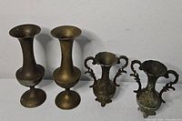 Two trumpet brass bud vases and two ornate urn vases on white surface