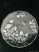 Top view of clear glass cake stand showing etched poppy design and scalloped rim