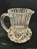 Front view of clear pressed glass creamer showing ribbed body, handle and diamond hobnail base