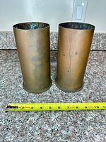 Two brass shell casings with measuring tape showing height