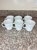 Six white Corning mugs grouped on countertop
