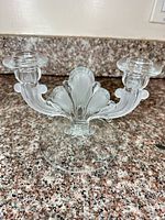 Front view of clear glass two-arm candelabra with frosted center and round base displayed on countertop