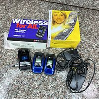 Three LG flip phones, two retail boxes, chargers and cables displayed on countertop