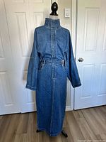 Front view of blue denim dress on mannequin showing high collar, waist belt, full length