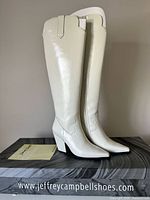 Side view of both white leather knee-high boots standing on branded box