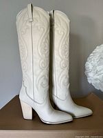 Side view of both ivory embroidered knee-high boots standing upright