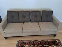 Front view of beige three-seat sofa with four dark accent cushions