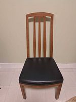 Front view of wooden dining chair, black padded seat