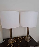 Pair of matching metal table lamps with white drum shades on table