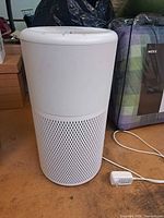 Front view of Noma white cylindrical air purifier with power adapter
