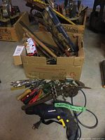 Overview of entire lot showing drill, pliers, screwdrivers, auger bits and other tools on floor in front of box