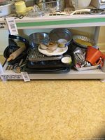 Full view of stacked bakeware items on shelf showing muffin pan, baking sheets, cooling rack, cake pans, measuring cups, rolling pin, pot holders