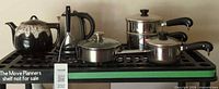 Group shot of teapot, electric kettle, three saucepans and lids on shelf