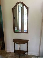 Wall-mounted arched wood mirror above demilune table