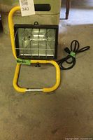 Front view of halogen work light showing yellow stand, black housing, grille, cord