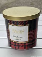 Front of candle showing Motif label, plaid design and gold lid