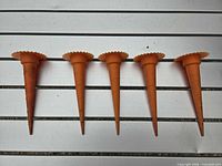 Five orange plastic plant watering spikes lined up on a slatted surface