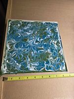 Front view of square acrylic pour painting with tape measure showing size
