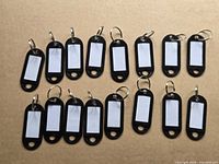 All 15 black plastic key tags arranged on surface showing front with white inserts