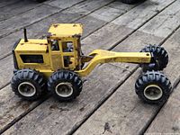 Left-side view of yellow Tonka grader showing six rear wheels, articulated arm and general wear
