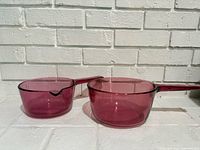 Both cranberry glass saucepans side by side showing size difference and condition