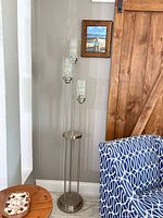 Full view of brushed nickel three-light floor lamp beside chair