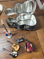 All items laid out: metal case, three loose miniature guitars, cased miniature guitar, motorcycle