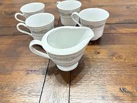 Pitcher, creamer and four cups grouped on wooden surface