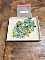 Tray containing multicolored glass marbles and empty zip bag