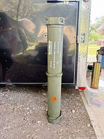 Full view of olive drab 105 mm ammunition tube standing upright