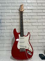 Full front view of red electric guitar leaning against white brick wall