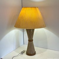 Full view of lamp showing jute-wrapped hourglass base and pleated shade illuminated