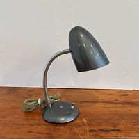 Side view of grey metal gooseneck desk lamp showing shade, neck, base and cord
