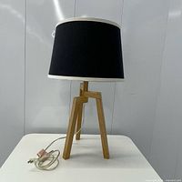 Full view of lamp showing wood tripod base, black shade, cord