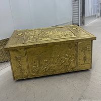 Front and side view of brass-clad chest showing embossed scenes and torch motifs