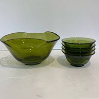 Large olive green serving bowl beside stack of four matching bowls on white background