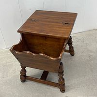 Angled view showing closed hinged lid, magazine rack front, turned legs and stretcher