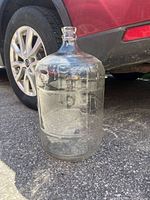 Full view of clear glass carboy beside vehicle