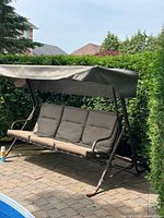 Full view of metal porch swing with canopy by hedge