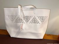 Front view of white tote showing perforated design and straps with tag attached