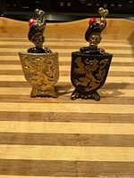 Front view of both bottle openers seated in their matching shield stands on striped surface