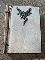 Front cover showing handmade paper texture, wood spine strip, blue cord stitch, and metal fairy