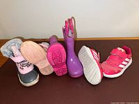 Three pairs of kids shoes aligned showing outer view: winter boots, rain boots, Adidas sneakers