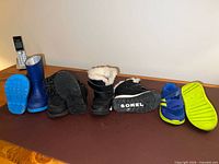 All four pairs lined up: blue rain boots, black casual boots, black Sorel snow boots, blue/green sneakers