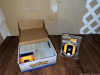 Bulk Pokemon cards in open cardboard Pokemon box beside sealed Ultra Ball stationery set