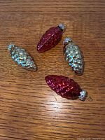 All four red and gold glass pinecone ornaments on wood surface