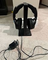 Headphones resting on stand with cable and power adapter on carpet