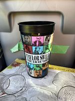 Front view of black plastic Taylor Swift The Eras Tour souvenir tumbler showing multicolor graphic tiles and logo text