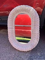 Front view of white oval wicker wall mirror leaning against vehicle