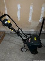 Full side view of Yardworks corded electric snow thrower showing handle, wheels and body